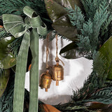 A close-up shot of an Everlasting Wreath with striking contrast between the traditional, needle-like texture of preserved Cedar and the large, smooth, often bi-coloured leaves of preserved Magnolia. A soft green velvet bow is thoughtfully tied in the top left corner, adding a subtle touch of richness and colour. The design is perfected by the gentle chime of two small vintage iron bells, which hang suspended in the centre by natural jute rope.