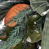 A close-up shot of an Everlasting Wreath with striking contrast between the traditional, needle-like texture of preserved Cedar and the large, smooth, often bi-coloured leaves of preserved Magnolia. A soft green velvet bow is thoughtfully tied in the top left corner, adding a subtle touch of richness and colour. 