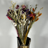 This magnificent, hand-tied bouquet is a vibrant symphony of contrasting colours and textures designed for the sophisticated interior. The Amethyst base of lush purple Statice provides a dramatic backdrop for the Gold accents: bright yellow Achillea Parker and soft natural pink Helichrysums. Textural elements featuring the unique, wavy shapes of red coral Celosia and Phalaris dyed in three complementary colors (natural, orange, and red).