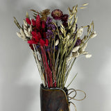 This magnificent, hand-tied bouquet is a vibrant symphony of contrasting colours and textures designed for the sophisticated interior. The Amethyst base of lush purple Statice provides a dramatic backdrop for the Gold accents: bright yellow Achillea Parker and soft natural pink Helichrysums. Textural elements featuring the unique, wavy shapes of red coral Celosia and Phalaris dyed in three complementary colors (natural, orange, and red).