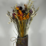 This magnificent, hand-tied bouquet is a vibrant symphony of contrasting colours and textures designed for the sophisticated interior. The Amethyst base of lush purple Statice provides a dramatic backdrop for the Gold accents: bright yellow Achillea Parker and soft natural pink Helichrysums. Textural elements featuring the unique, wavy shapes of red coral Celosia and Phalaris dyed in three complementary colors (natural, orange, and red).