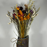 This magnificent, hand-tied bouquet is a vibrant symphony of contrasting colours and textures designed for the sophisticated interior. The Amethyst base of lush purple Statice provides a dramatic backdrop for the Gold accents: bright yellow Achillea Parker and soft natural pink Helichrysums. Textural elements featuring the unique, wavy shapes of red coral Celosia and Phalaris dyed in three complementary colors (natural, orange, and red).