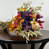 This magnificent, hand-tied bouquet is a vibrant symphony of contrasting colours and textures designed for the sophisticated interior. The Amethyst base of lush purple Statice provides a dramatic backdrop for the Gold accents: bright yellow Achillea Parker and soft natural pink Helichrysums. Textural elements featuring the unique, wavy shapes of red coral Celosia and Phalaris dyed in three complementary colors (natural, orange, and red).