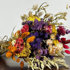 This magnificent, hand-tied bouquet is a vibrant symphony of contrasting colours and textures designed for the sophisticated interior. The Amethyst base of lush purple Statice provides a dramatic backdrop for the Gold accents: bright yellow Achillea Parker and soft natural pink Helichrysums. Textural elements featuring the unique, wavy shapes of red coral Celosia and Phalaris dyed in three complementary colors (natural, orange, and red).
