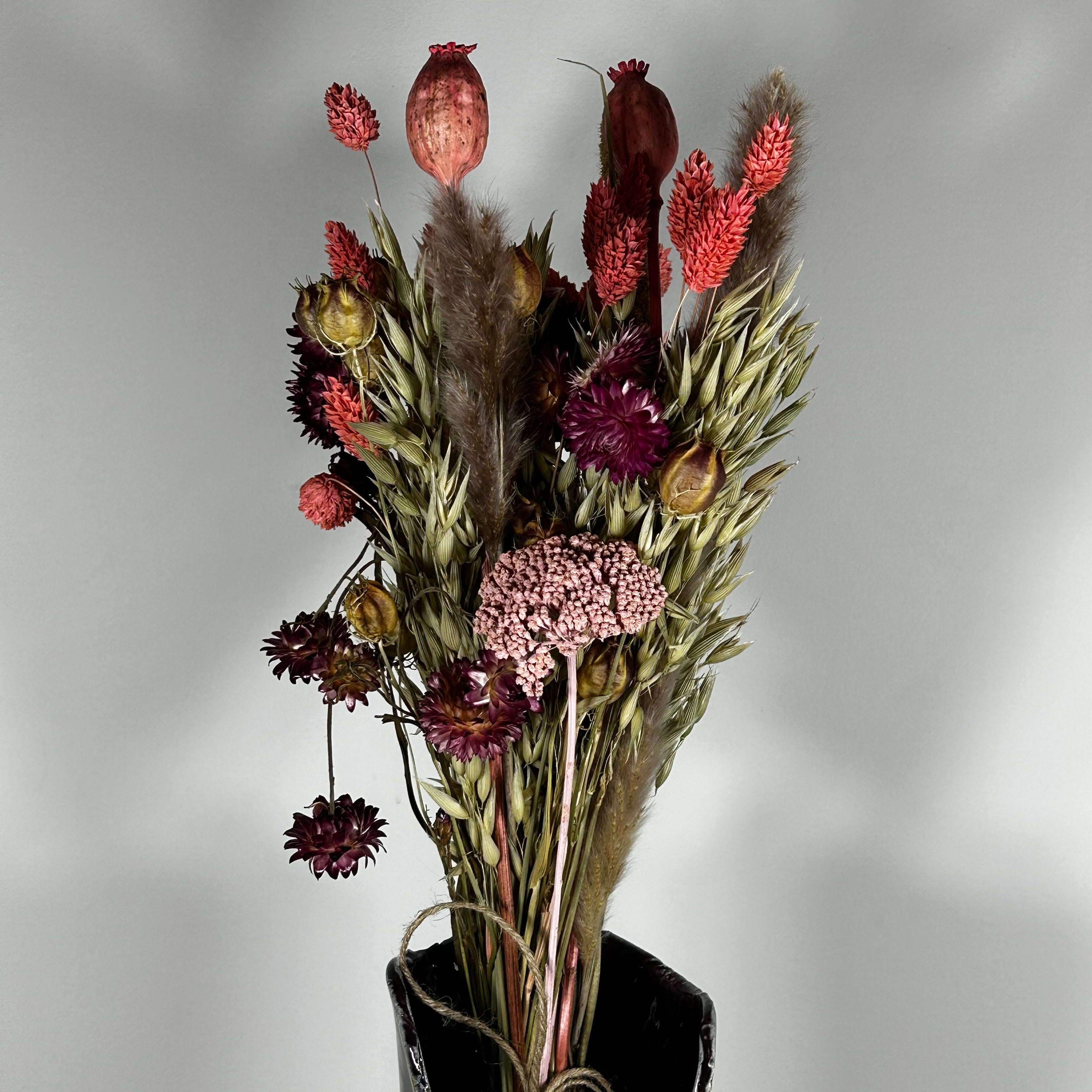 A hand-tied bouquet features the majestic, airy softness of natural Pampas Grass, contrasted with the deep, plush tones of deep burgundy Helichrysums.
The palette is enhanced by soft natural pink Helichrysums and vibrant dyed pink Achillea Parker, while coral-dyed Phalaris adds vertical movement. The rustic charm of burgundy Nigella seed pods, textured Poppy seed pods, and Quaker Oats provides intricate detail.