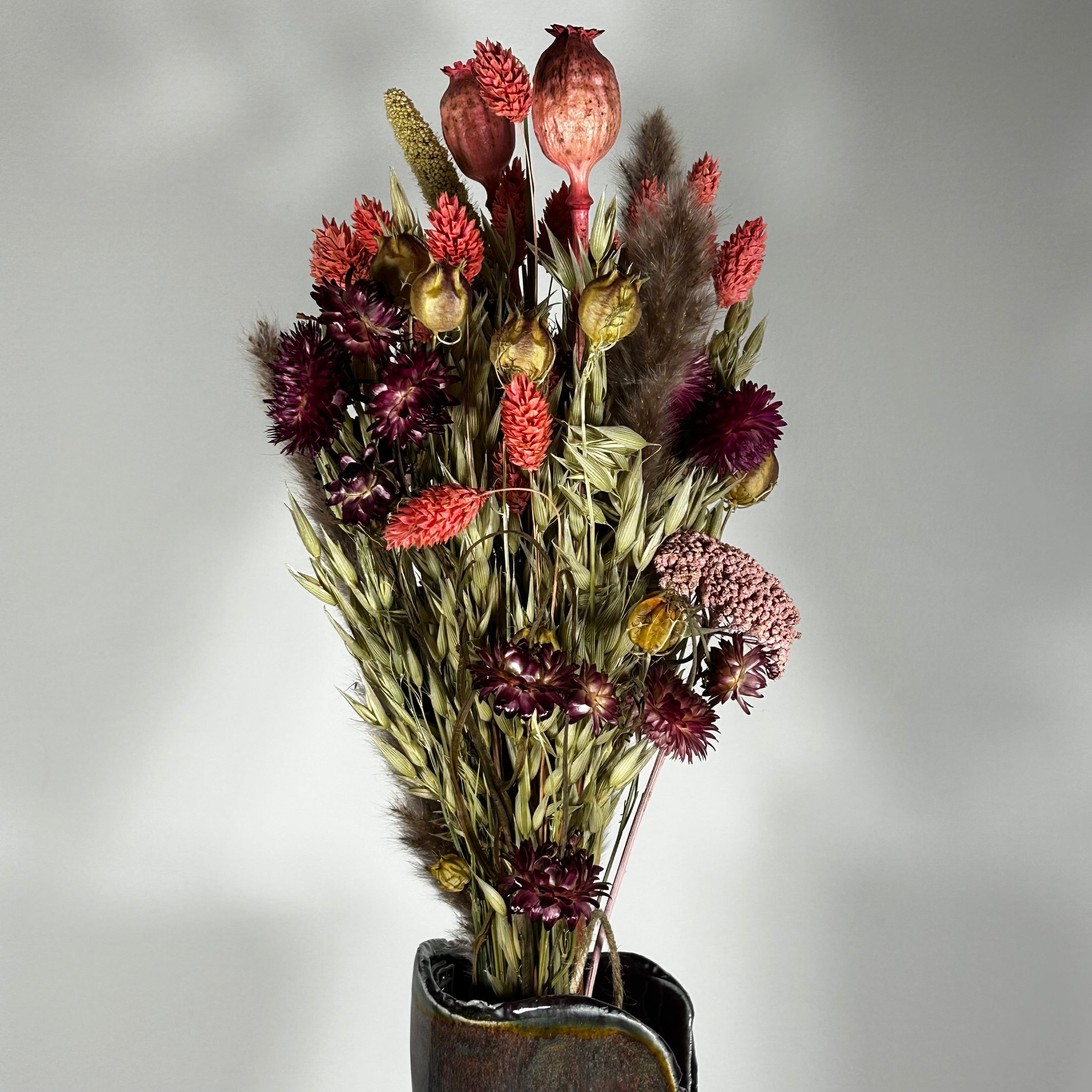 A hand-tied bouquet features the majestic, airy softness of natural Pampas Grass, contrasted with the deep, plush tones of deep burgundy Helichrysums.
The palette is enhanced by soft natural pink Helichrysums and vibrant dyed pink Achillea Parker, while coral-dyed Phalaris adds vertical movement. The rustic charm of burgundy Nigella seed pods, textured Poppy seed pods, and Quaker Oats provides intricate detail.