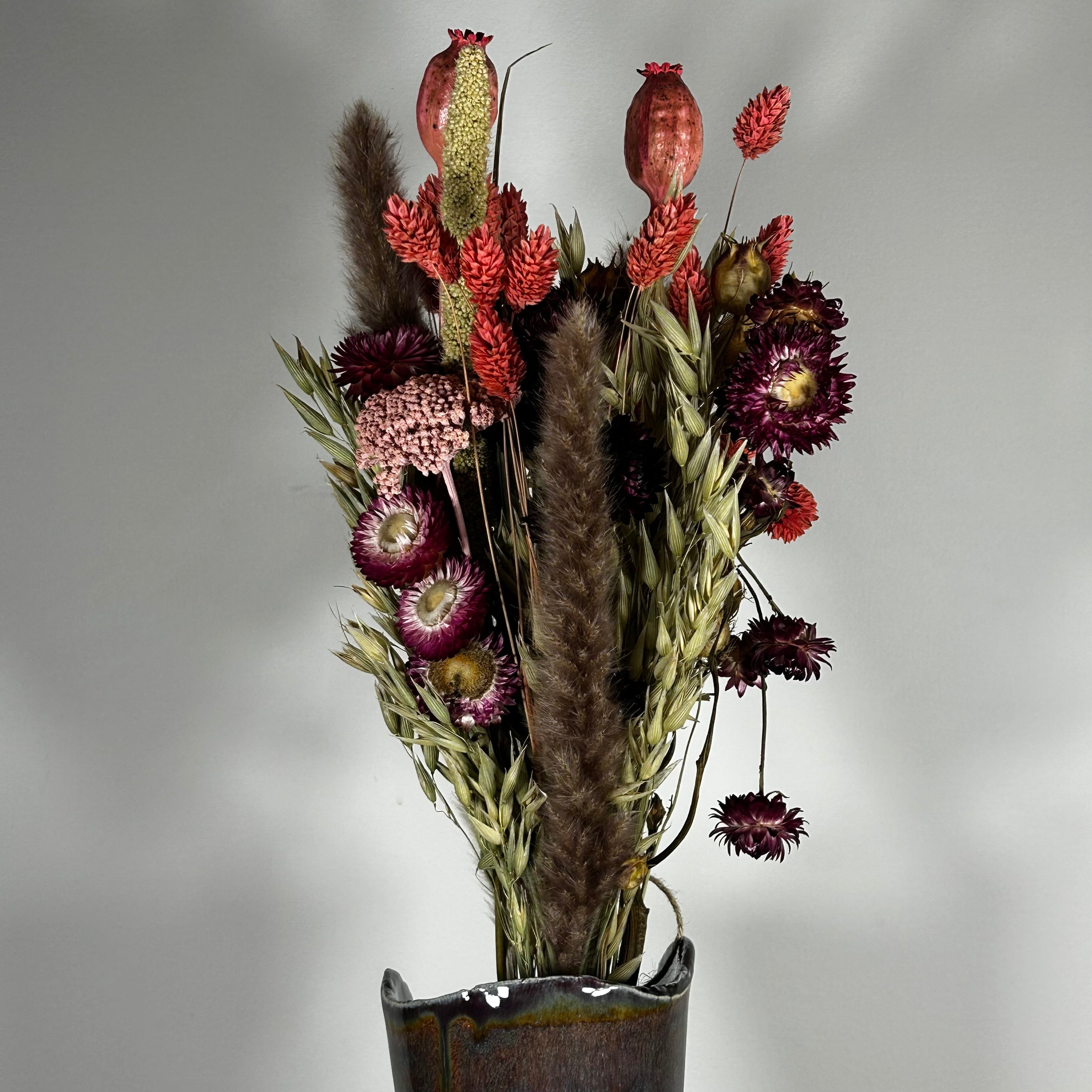 A hand-tied bouquet features the majestic, airy softness of natural Pampas Grass, contrasted with the deep, plush tones of deep burgundy Helichrysums.
The palette is enhanced by soft natural pink Helichrysums and vibrant dyed pink Achillea Parker, while coral-dyed Phalaris adds vertical movement. The rustic charm of burgundy Nigella seed pods, textured Poppy seed pods, and Quaker Oats provides intricate detail.