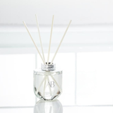 Glass diffuser bottle with silver trim, with scent sticks on a white background