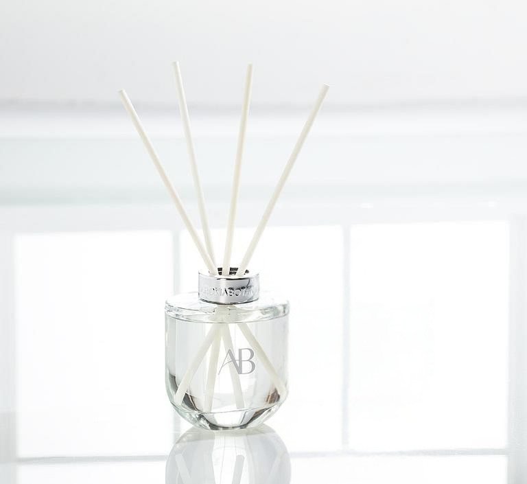 Glass diffuser bottle with silver trim, with scent sticks on a white background