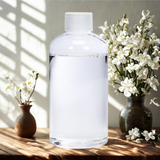Clear glass bottle on a wooden surface with white flowers in the background