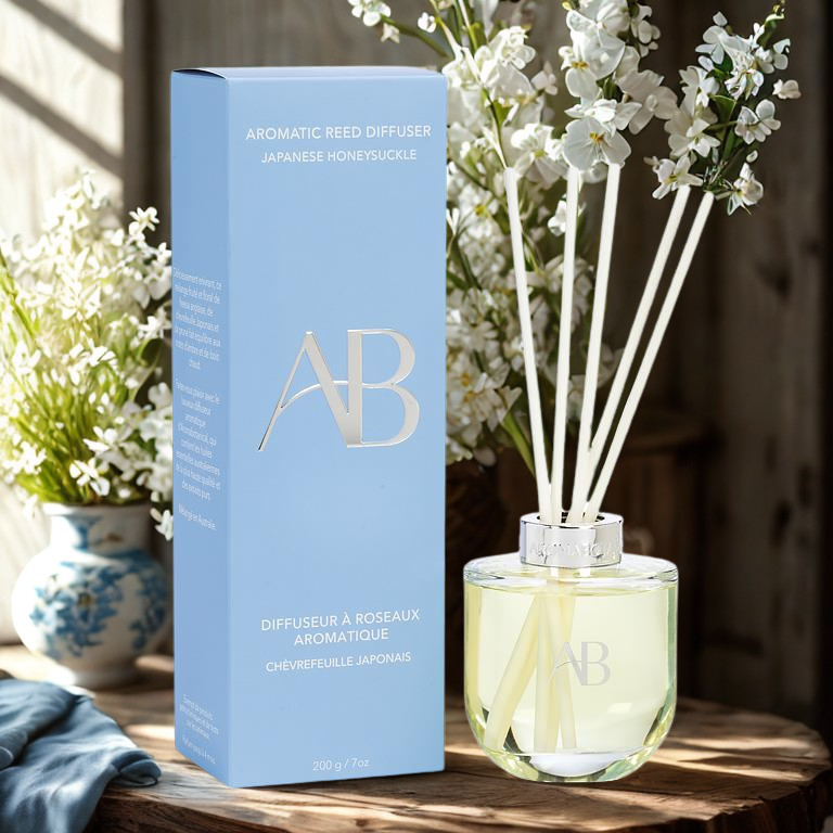 Aromatic reed diffuser on a wooden surface with flowers in the background.