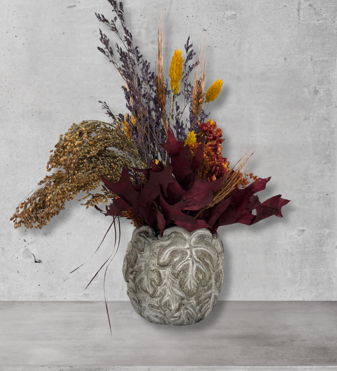 Decorative arrangement of dried flowers in a textured vase on a concrete surface.