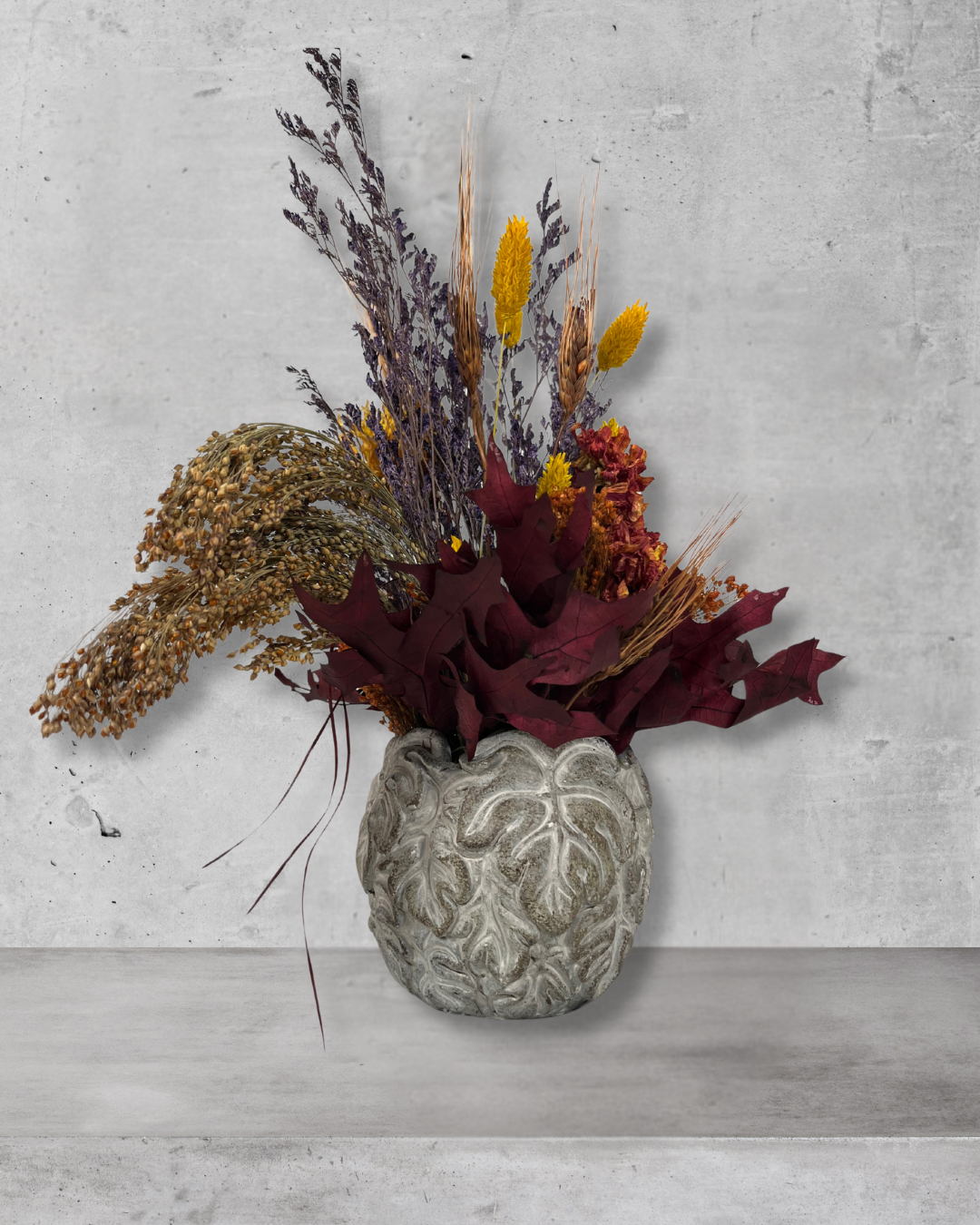 Decorative arrangement of dried flowers in a textured vase on a concrete surface.