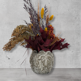 Decorative arrangement of dried flowers in a textured vase on a concrete surface.