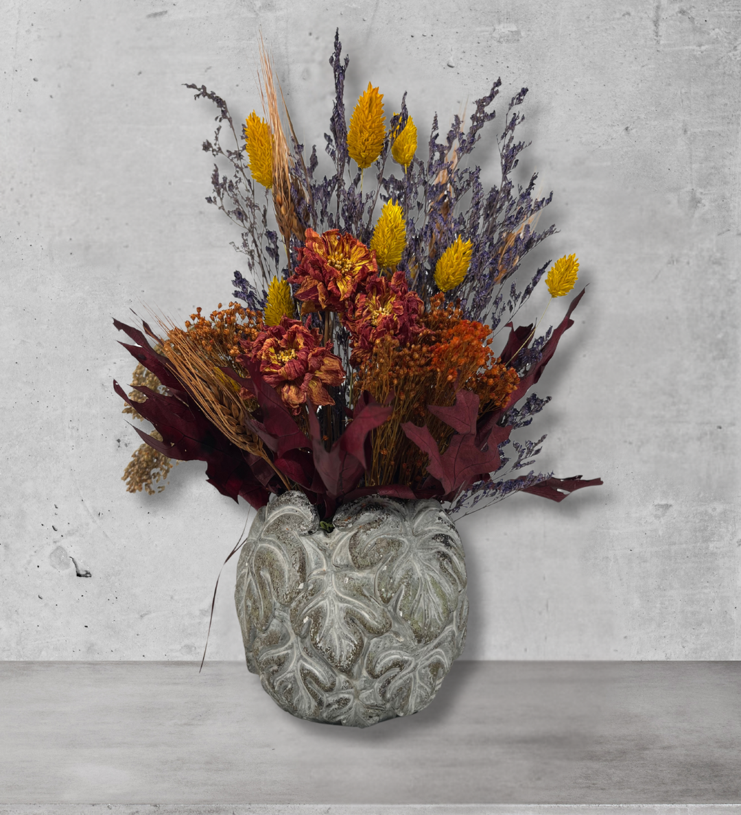 Decorative concrete vase with dried flowers in warm earthy colours against a concrete wall