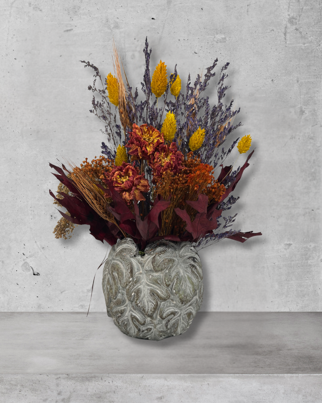 Decorative concrete vase with dried flowers in warm earthy colours against a concrete wall