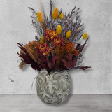 Decorative concrete vase with dried flowers in warm earthy colours against a concrete wall