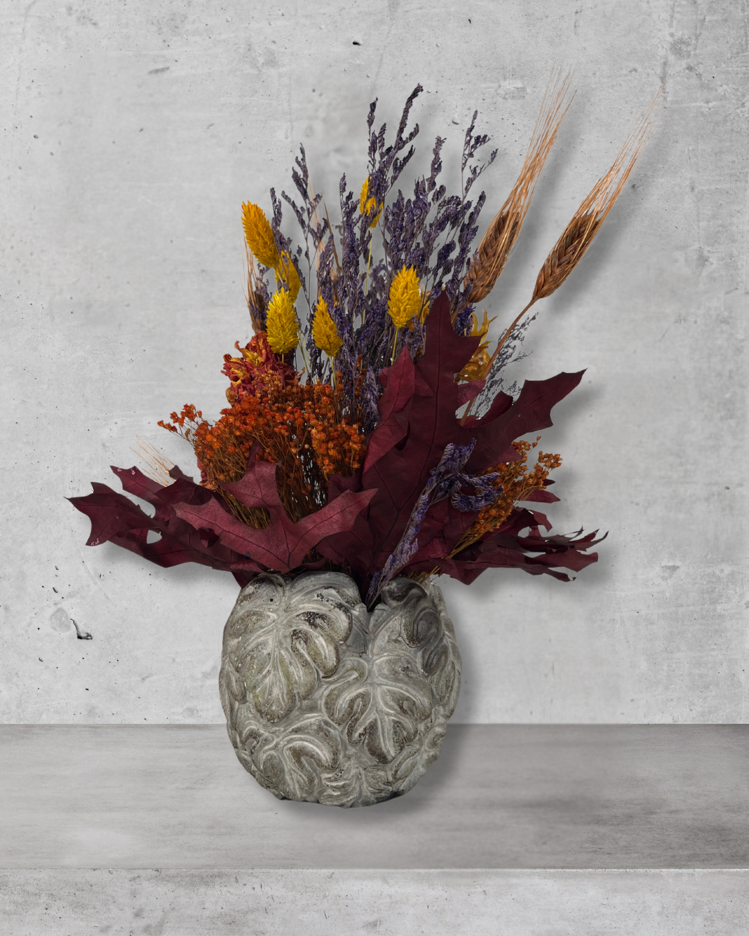Decorative concrete vase with dried flowers in warm earthy colours against a concrete wall