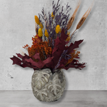Decorative concrete vase with dried flowers in warm earthy colours against a concrete wall