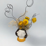 Decorative vase shaped like a face with dried flowers on a light grey background
