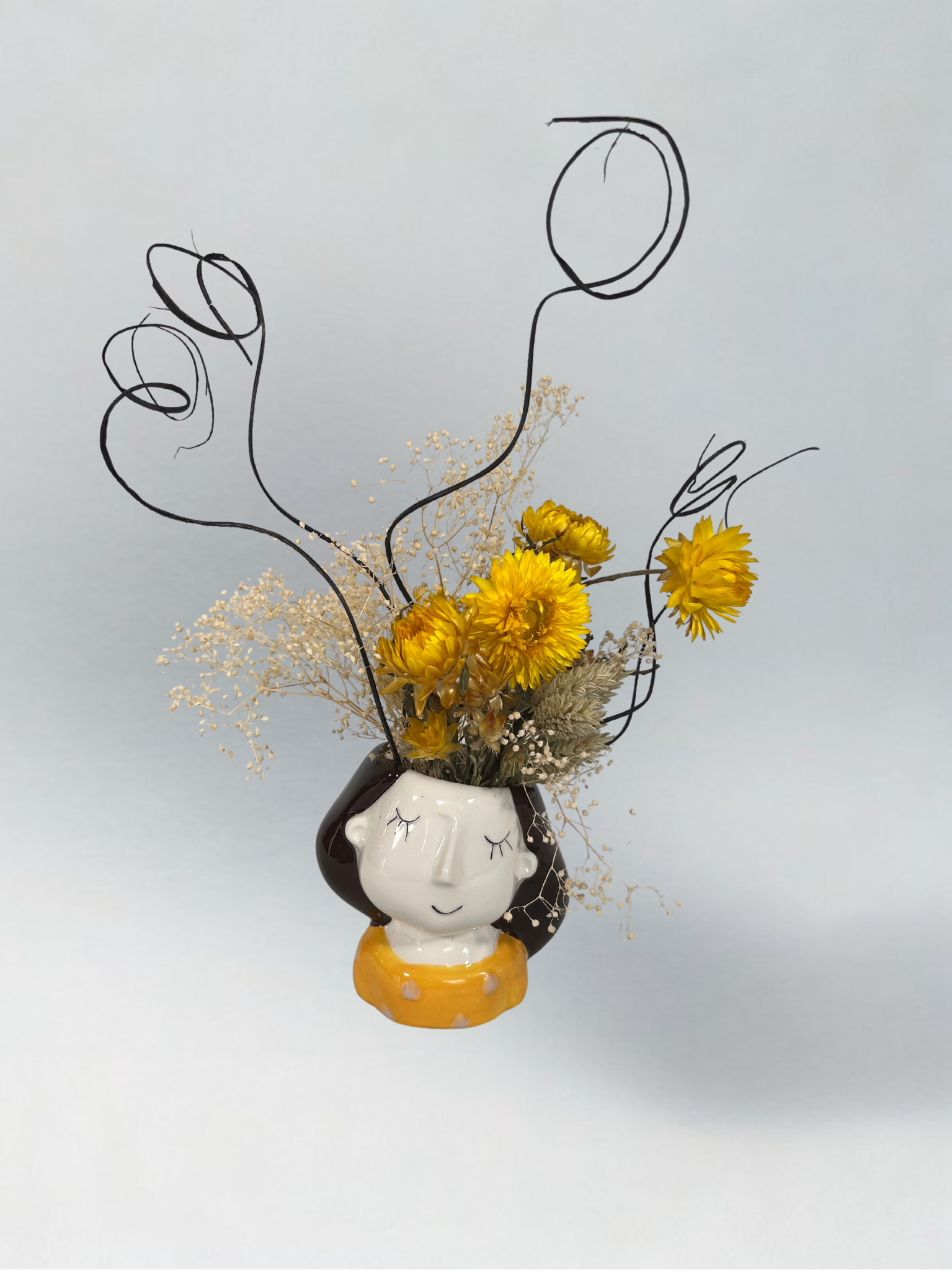 Decorative vase shaped like a face with dried flowers on a light grey background