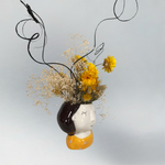 Decorative head-shaped vase with yellow flowers and brown curly ting ting accents on a light grey background