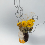 Decorative vase with yellow flowers and brown curly ting ting on a light grey background