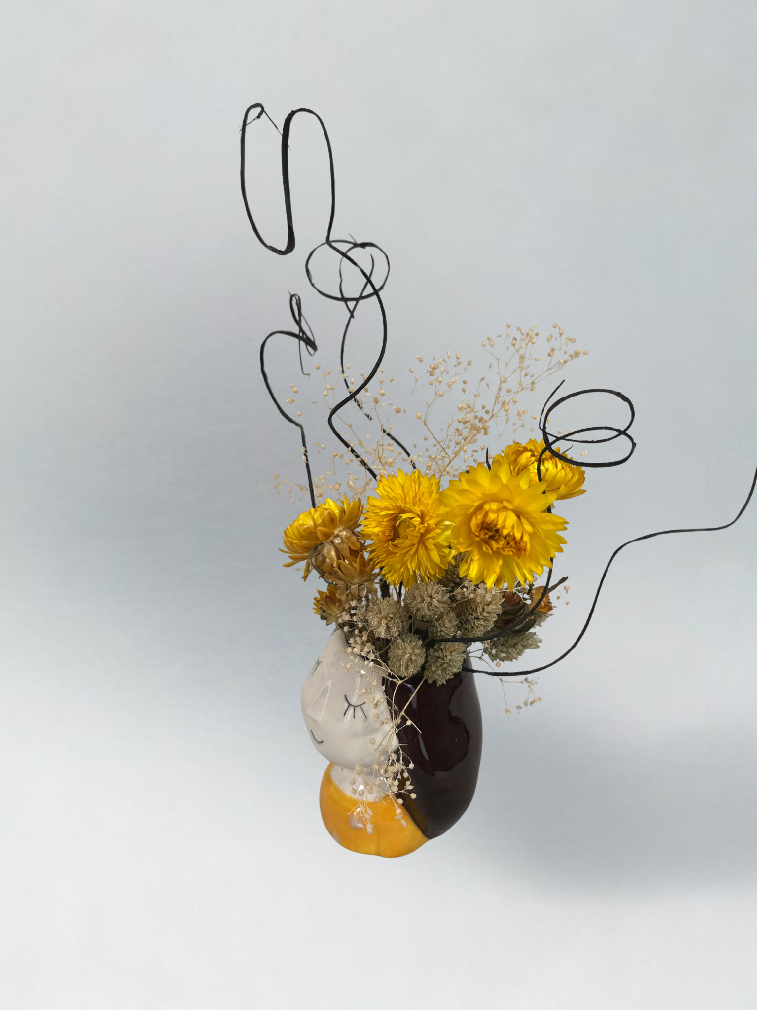 Decorative vase with yellow flowers and brown curly ting ting on a light grey background