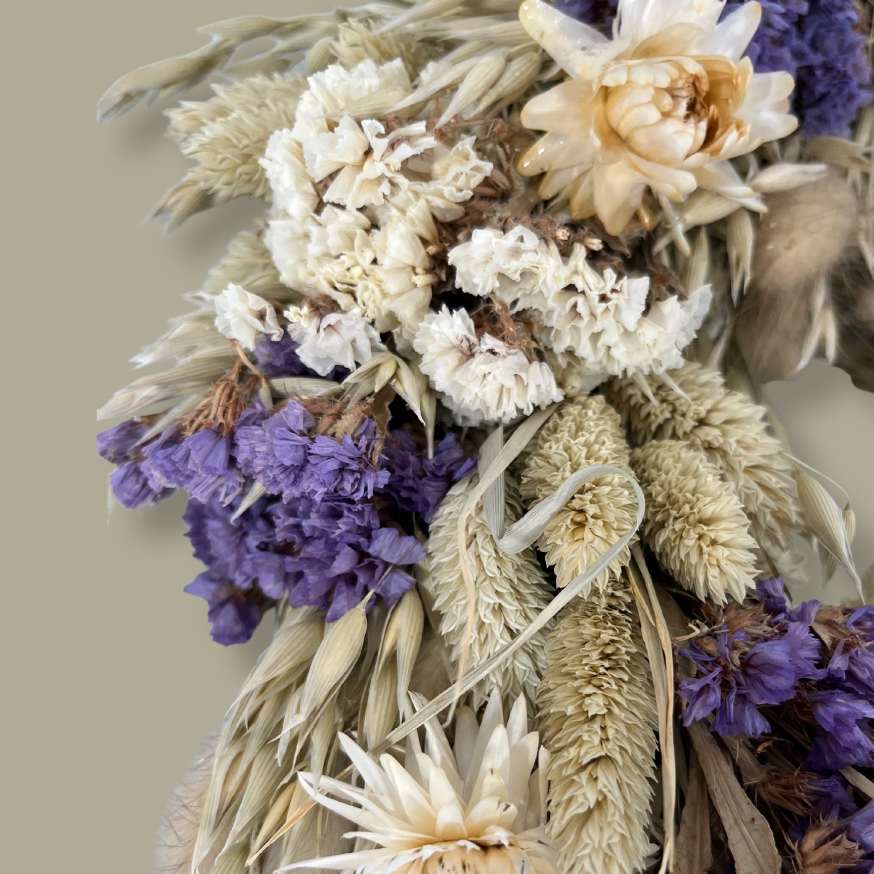 Close-up view of the right side of a 10-inch wreath made with lush purple Statice, creamy natural strawflowers, feathery bunny tails, delicate Larurus ovatus, and graceful natural oat grass. 