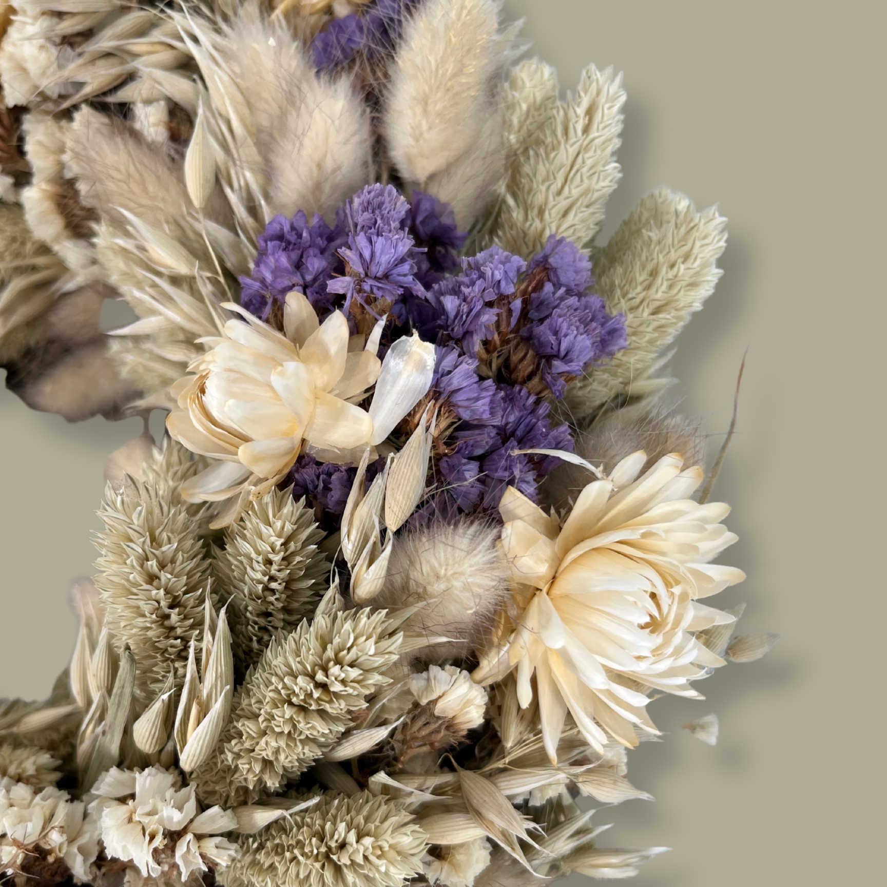 Close-up view of the left side of a 10-inch wreath made with lush purple Statice, creamy natural strawflowers, feathery bunny tails, delicate Larurus ovatus, and graceful natural oat grass. 