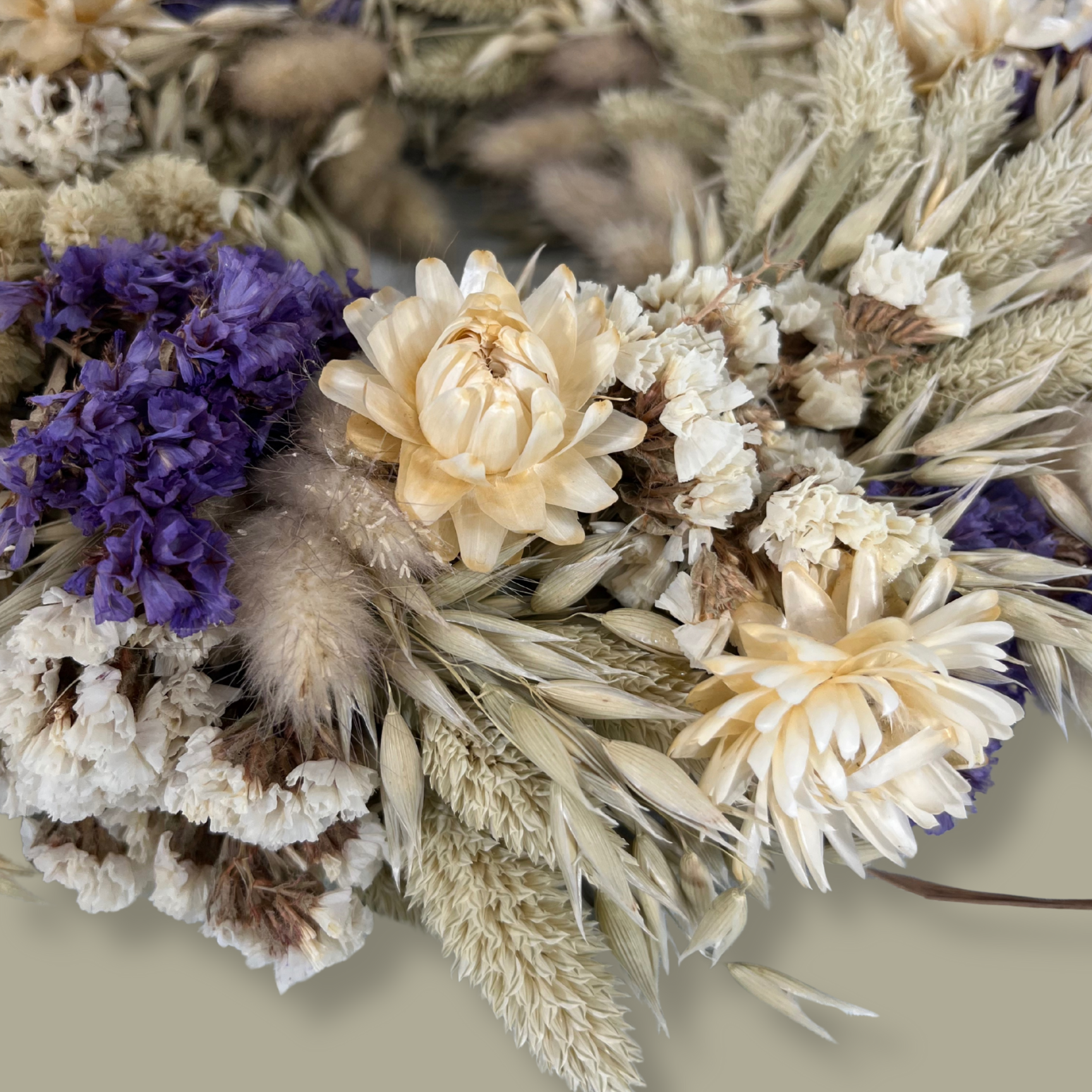 Close-up view of a 10-inch wreath made with lush purple Statice, creamy natural strawflowers, feathery bunny tails, delicate Larurus ovatus, and graceful natural oat grass. 