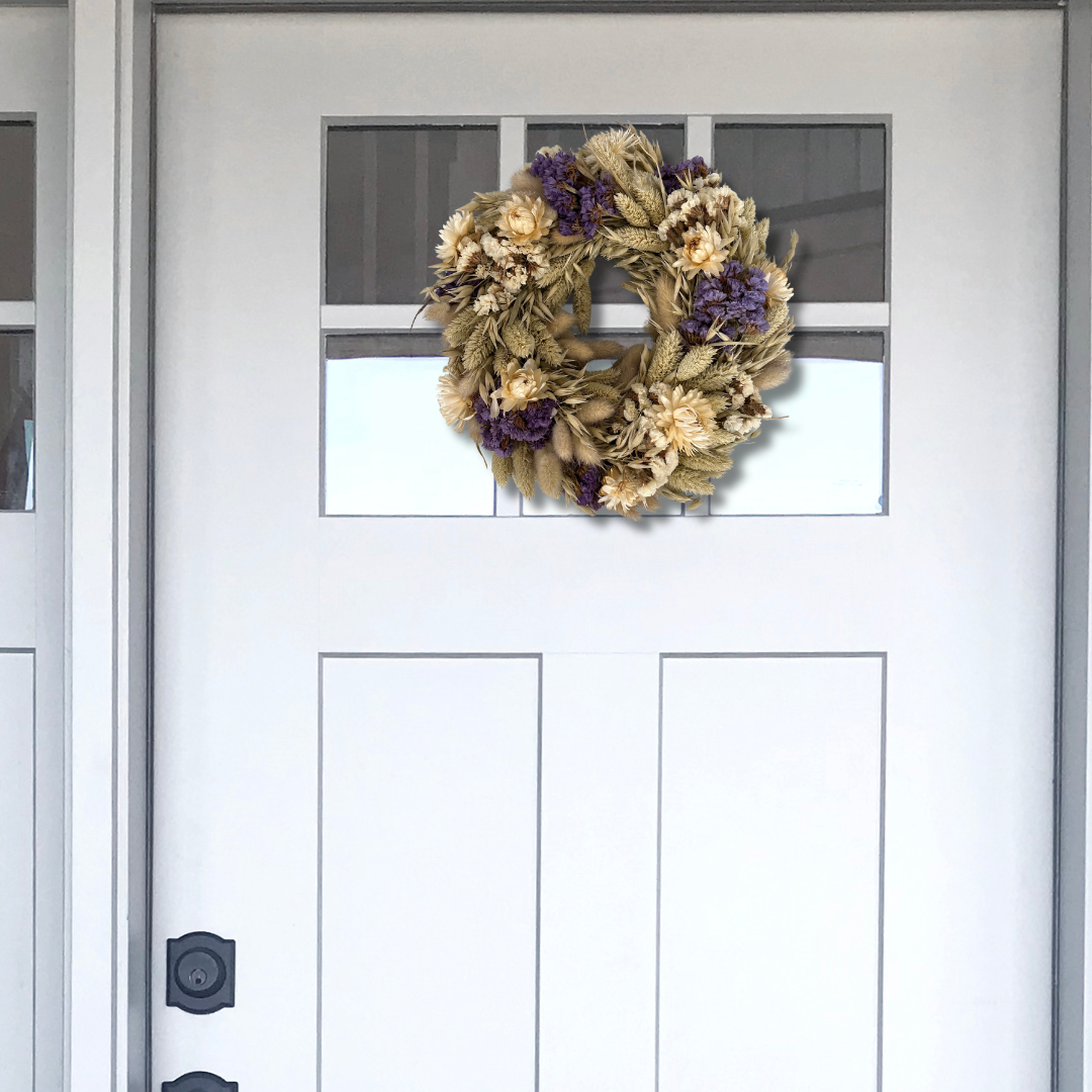 10-inch wreath made with lush purple Statice, creamy natural strawflowers, feathery bunny tails, delicate Larurus ovatus, and graceful natural oat grass on a white door with a window.