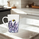 White mug with a floral design featuring lavender and a bee on a marble countertop in a kitchen.