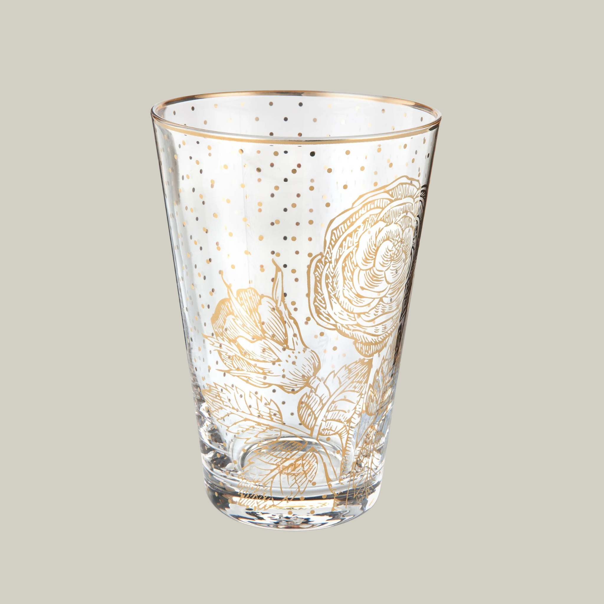Glass tumbler with gold floral and poke-a-dot design on a plain background