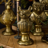 A decorative brass mouse bust figurine wearing round glasses, a bow tie, and a tuxedo jacket, displayed on a wooden surface with other ornate brass animal busts in the background.