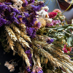 Close-up of decorative 30 inch dried floral wreath with vibrant statice and helichrysum and the whimsical texture of various grains, and curly ting ting on a dark background