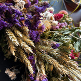Close-up of decorative 30 inch dried floral wreath with vibrant statice and helichrysum and the whimsical texture of various grains, and curly ting ting on a dark background