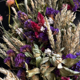 Close-up of decorative 30 inch dried floral wreath with vibrant statice and helichrysum and the whimsical texture of various grains, and curly ting ting on a dark background