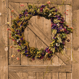 Decorative 30 inch dried floral wreath with vibrant statice and helichrysum and the whimsical texture of various grains, and curly ting ting on a wooden door.