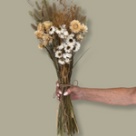 Bouquet of dried flowers held by a hand against a plain background