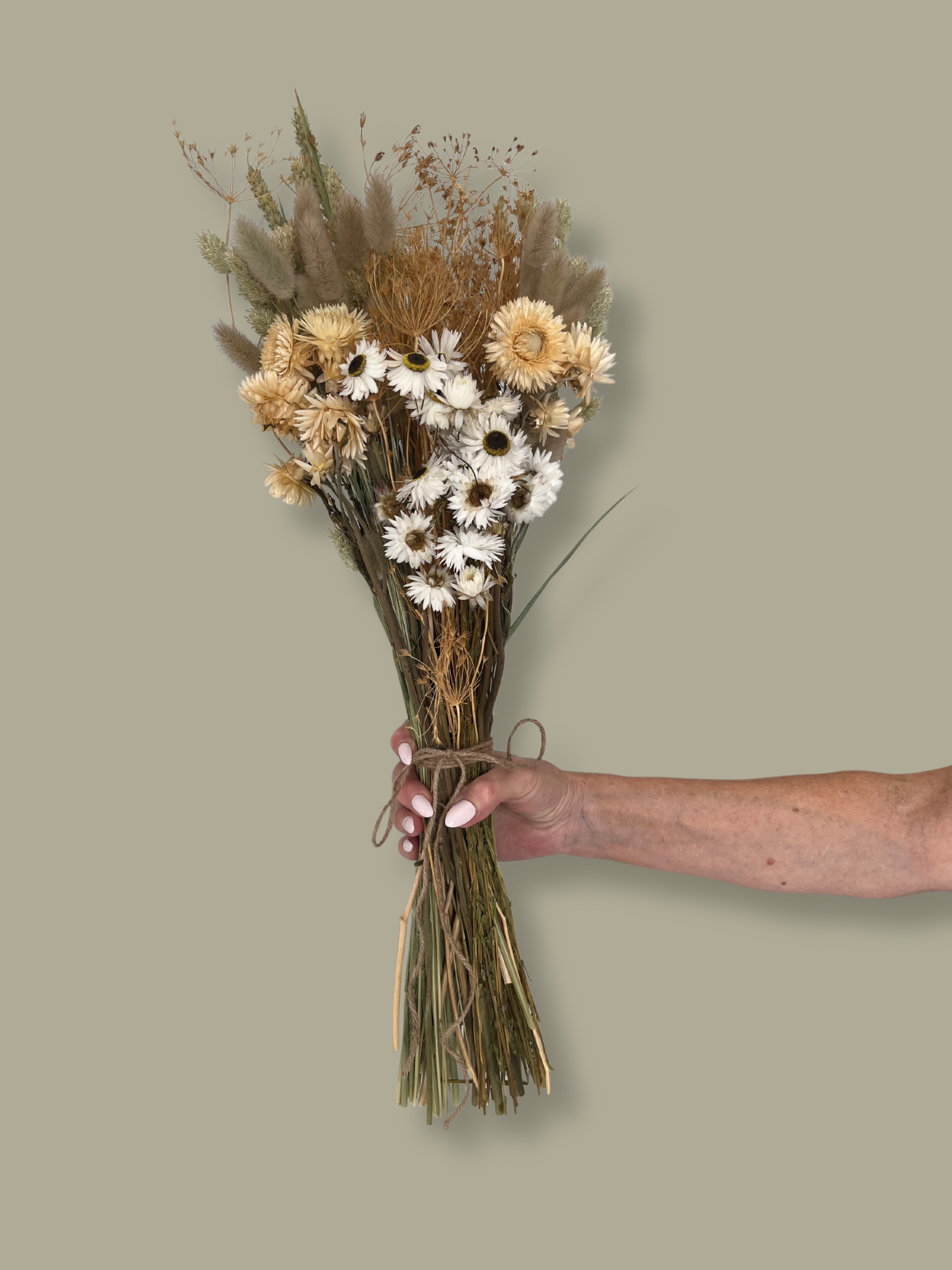 Bouquet of dried flowers held by a hand against a plain background