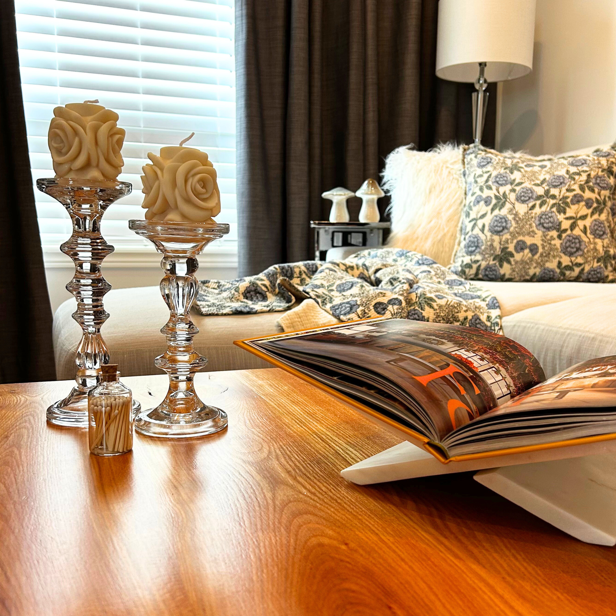Living room with two rose embossed candles on top of two beautiful glass traditionally styled candlestick holders on a wooden table.