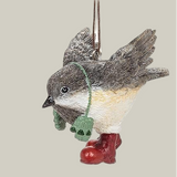Decorative winter chickadee ornament wearing green mittens on a string around it's neck and red boots on a pale green background