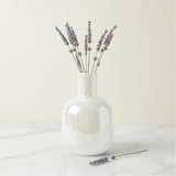 Mini bud vase features a sleek bottle shape and a rainbow lustre glass finish that catches the light beautifully. Shown here with sprigs of lavender on a white marble table with a white background.