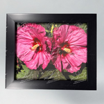 Matte black framed artwork of pink hibiscus flowers on a green leafy background