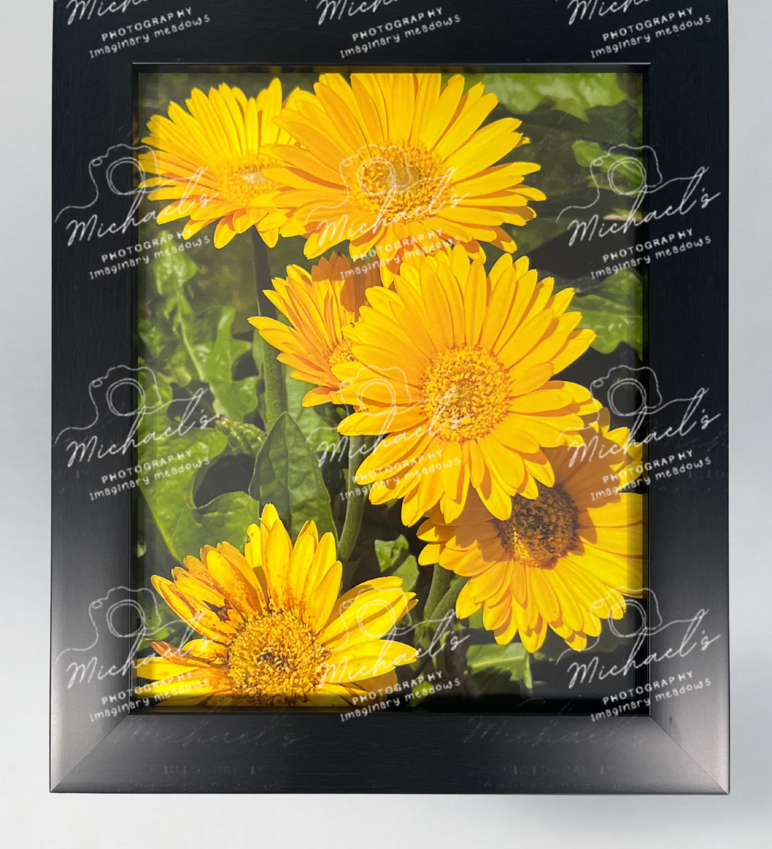 Black matte framed picture of yellow flowers with 'Michaels' branding on a gray background