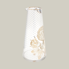 Glass handle-less pitcher with gold floral and poke-a-dot design on a soft green background