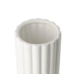 A close-up of the opening of a tall cylindrical vase, whose silhouette is softened by delicate vertical ribbing, creating subtle movement as light shifts across its glossy white surface. 