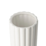 A close-up of the opening of a tall cylindrical vase, whose silhouette is softened by delicate vertical ribbing, creating subtle movement as light shifts across its glossy white surface. 