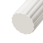 A close-up of the bottom of a tall cylindrical vase, whose silhouette is softened by delicate vertical ribbing, creating subtle movement as light shifts across its glossy white surface. 